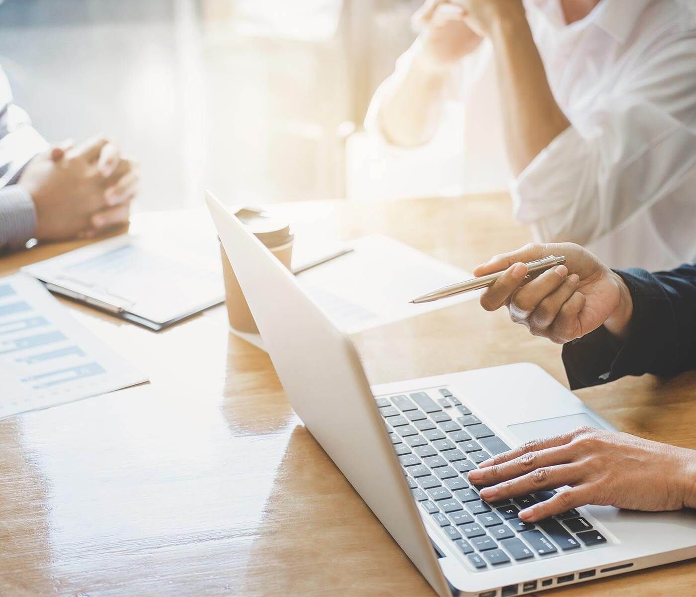 Close-up van handen die een laptop en pen gebruiken tijdens een vergadering.
