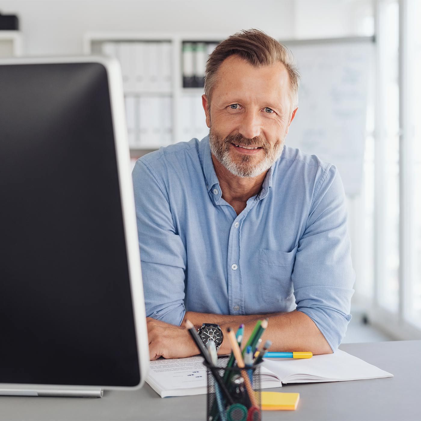 Lachende man met baard, zittend aan zijn bureau 