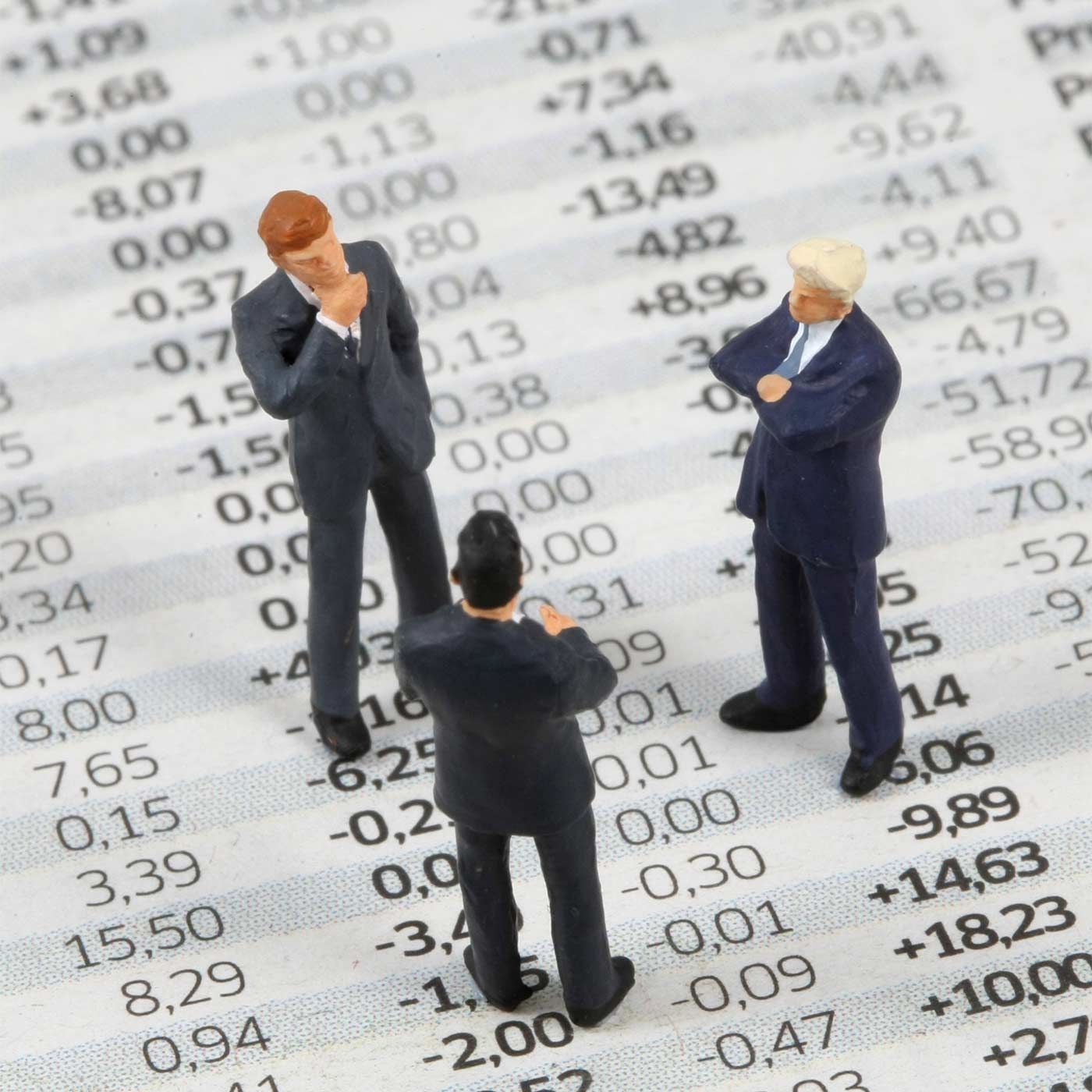 Drie kleine figuurtjes van zakenmensen staan op een beursoverzicht.