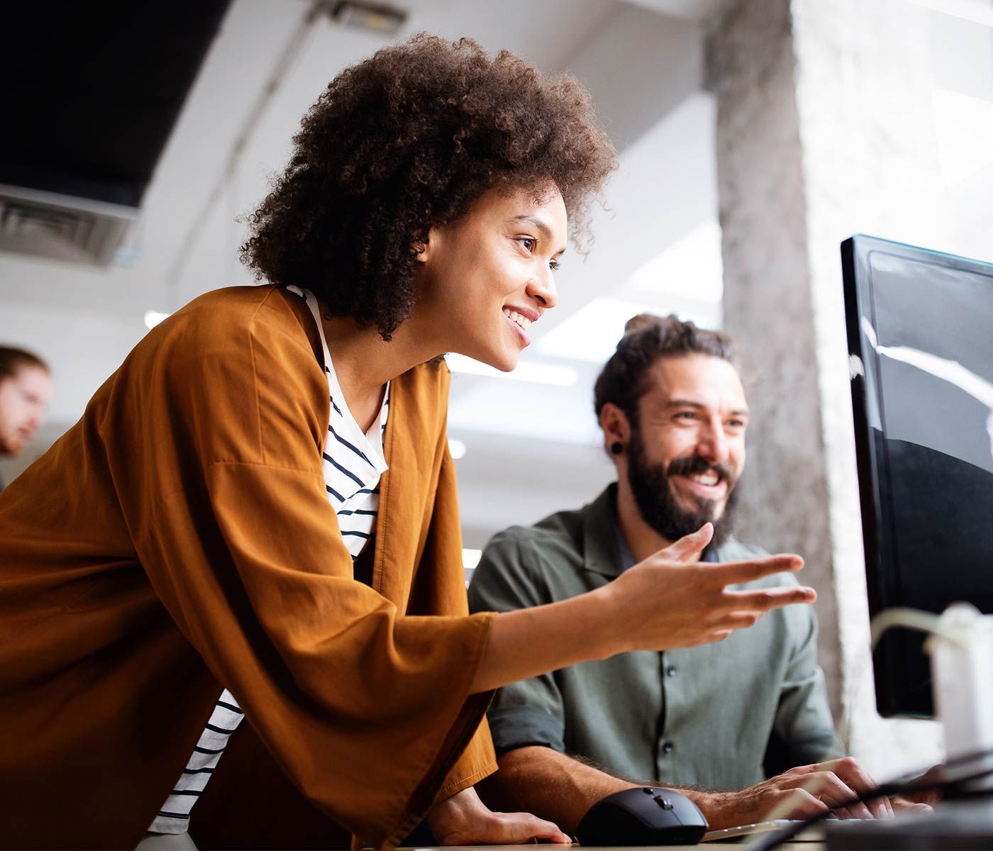 Twee glimlachende collega's werken samen aan de computer op kantoor.
