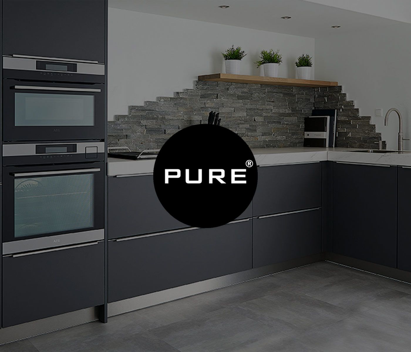Moderne donkere keuken met stenen wand en PURE-logo.